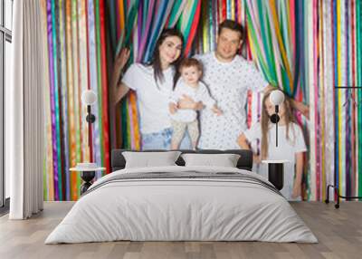 Happy family mother, father and two children stretching out her hands at celebration party on colourful rainbow ribbons background Birthday or New Year eve celebrating concept. Wall mural