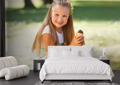 laughing child girl with ice cream sitting on grass in the park on a hot summer day Wall mural