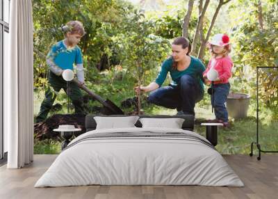 Mother and two children brother and sister planting tree in a garden.. Wall mural