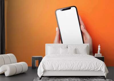 A female person holding a mobile phone with blank white display screen on an orange background. Smartphone mockup template Wall mural