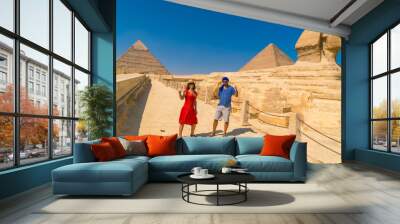 A tourist couple at The Great Sphinx of Giza and in the background the Pyramids of Giza, the oldest Funerary monument in the world. In the city of Cairo, Egypt Wall mural