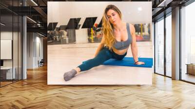 Lifestyle training in a gym, sport and health wellness. Pretty blonde girl of Caucasian ethnicity performing gymnast stretching Wall mural