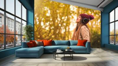 Portrait of a woman in autumn in a forest with brown leaves with her eyes closed listening to music with headphones Wall mural