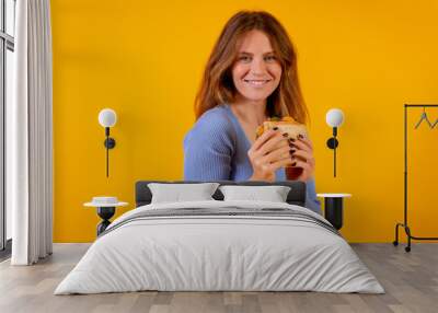 Portrait of woman eating a sandwich on a yellow background, healthy and vegetarian food Wall mural