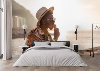 Sunset of a black ethnic man enjoy summer vacation on the beach eating an ice cream with a hat Wall mural