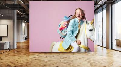 A happy young beautiful cheerful girl goes to school on her fairy tale white unicorn. Abstract concept on a pastel pink background. Education is more beautiful in imagination. Wall mural