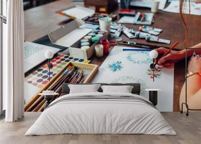 Close-up of female designer drawing floral compositions with crayons sitting at workplace surrounded with paint, gouache, brushes and other art supplies Wall mural