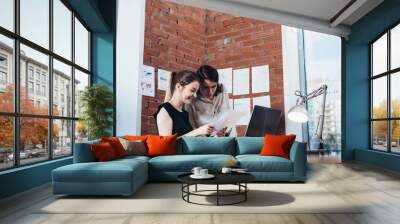 Smiling female colleagues reading paper documents sitting in the office Wall mural