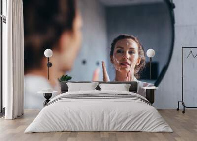 Woman washes in front of the mirror, applying foam to her face Wall mural