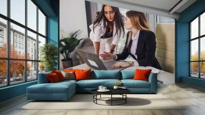 Young female assistant consulting with a top manager showing data on laptop screen and asking for advice sitting at working place Wall mural