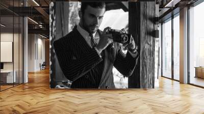 Black-white portrait of young beautiful fashionable man in classic suit with retro photo camera.
 Wall mural