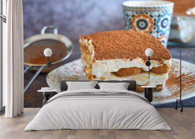 Square slice of tiramisu cake and a cup of coffee in the background, homemade gluten-free Italian layered dessert with ladyfinger biscuit and mascarpone cream decorated with cocoa powder Wall mural