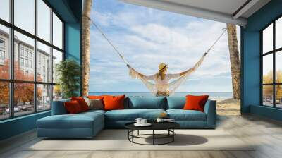 Woman in hat sitting in hammock on the beach. Travel and vacation concept. Wall mural