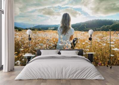 Young woman sitting on the chamomiles field and looking at the cloudy sky. Wall mural