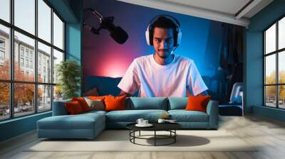 Young confident Asian man playing online computer video game, colorful lighting broadcast streaming live at home. Gamer lifestyle, E-Sport online gaming technology concept Wall mural