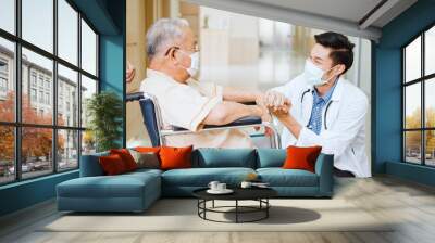 Young male Asian doctor crouch down holding hand and talk to the senior adult patient on wheelchair in hospital hallway. Medical healthcare job, or hospital business concept Wall mural