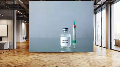 A bottle of a clear medicine herpes vaccine along with a syringe and surgical gloves on a plain surface Wall mural