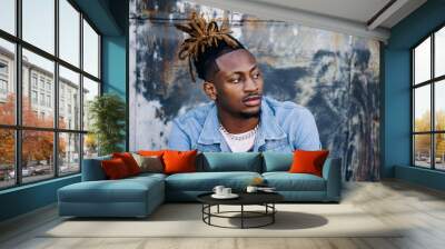 Handsome African-American Young man wearing a denim jacket with dreadlocks and facial hair and looking away off to the side Wall mural