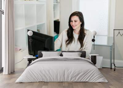 smiling brunette woman working on a computer in a small mostly white modern home office  Wall mural