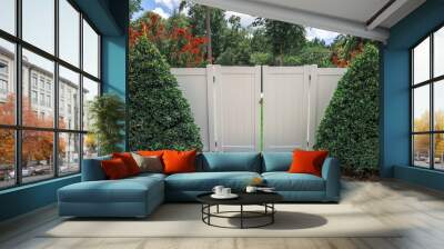 The opening to a white PVC tall fence for a backyard with sculpted and landscaped bushes on each side Wall mural