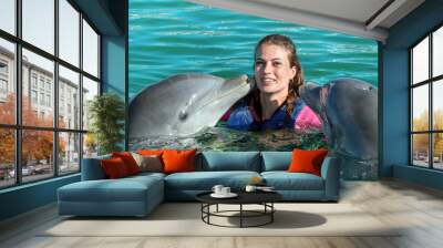 Dolphins kiss young woman in blue water. Smiling woman swimming with dolphin. Blue ocean water background. Wall mural