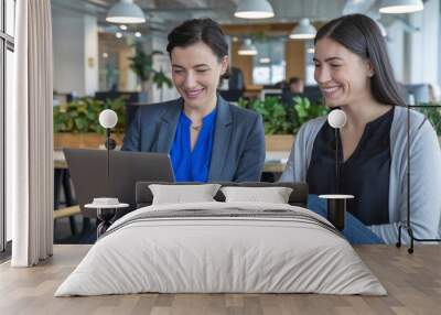 Two professional women collaborate on a project, smiling while working together on a laptop. Wall mural