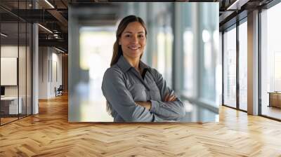 A Hispanic female facility manager stands with crossed arms, exuding confidence and approachability. She smiles warmly, set against a backdrop of a bright, modern corridor Wall mural