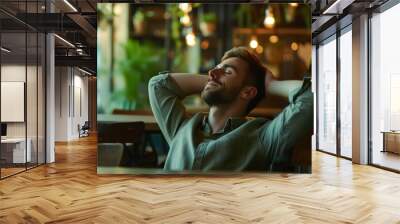 A relaxed young man enjoying tranquility in a cozy café surrounded by plants during the evening Wall mural