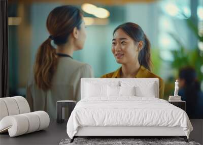 Two women engaged in a friendly conversation in a modern office setting during the afternoon Wall mural