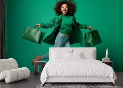 Very excited african american young adult woman happy jumping with shopping bags on green background. Payday delight. Studio portrait of cheerful girl carrying shoppers jumping for joy. Christmas Sale Wall mural