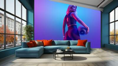 Confident fitness woman posing with a medicine ball. Attractive blonde sportswoman portrait holding with medicine fitness ball neon style creative light. Wall mural