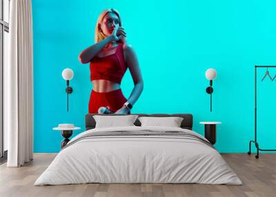 Young attractive sports girl in red sportswear on bright neon cyan background Wall mural