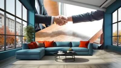 two businessmen make an agreement sitting and handshaking on wooden table in a meeting room Wall mural