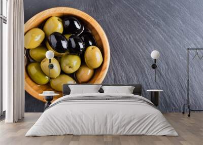 Black and green olives and oil in wooden bowl on black slate background. Top view with space for text. Wall mural