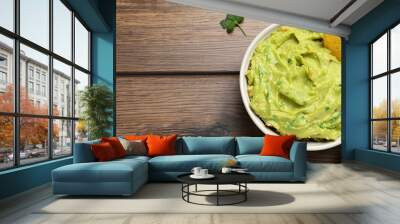 Bowl of delicious guacamole, lime and nachos chips on wooden table, top view. Space for text Wall mural