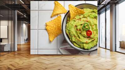 Bowl of delicious guacamole with chili pepper, nachos chips and lime on white tiled table, flat lay Wall mural