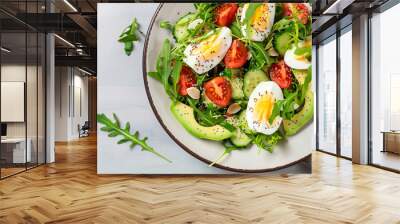 Tasty and healthy salad made of avocado, eggs, tomato, cucumber, cheese, arugula and chia seeds on a light plate. Top view. Flat lay. Banner. Wall mural