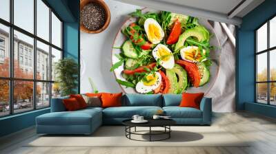 Tasty and healthy salad made of avocado, eggs, tomato, cucumber, cheese, arugula and chia seeds on a light plate. Top view. Flat lay. Banner. Wall mural