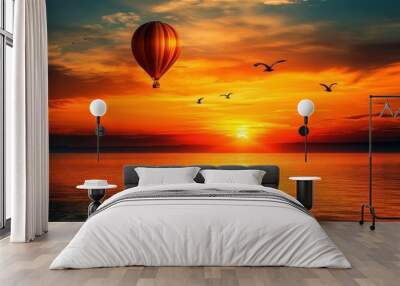 A hot air balloon floats across a vibrant sunset sky over a calm ocean with seagulls flying in formation. Wall mural