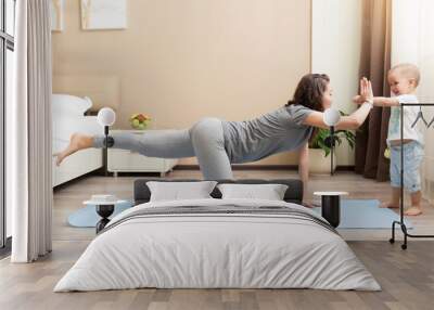 Beautiful young woman and little kid boy smiling while lying on yoga mat and doing fitness exercises at home Wall mural