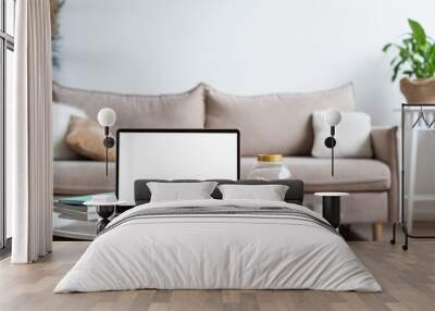 Laptop with blank white screen on the office table in home scandi interior. Stylish minimal workplace, copy space Wall mural