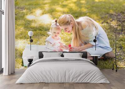 Portrait of happy young mother with little cute baby daughter spending time together in summer park looking at camera. Happiness, happy parenting and childhood concept Wall mural