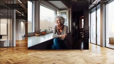 Smiling middle aged woman sitting in domestic kitchen at home, single mature senior in living room with flowers and plants Wall mural