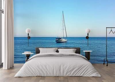 A Lone Sailboat Drifting Peacefully Across Calm Blue Waters Under a Clear Sky at Midday Wall mural