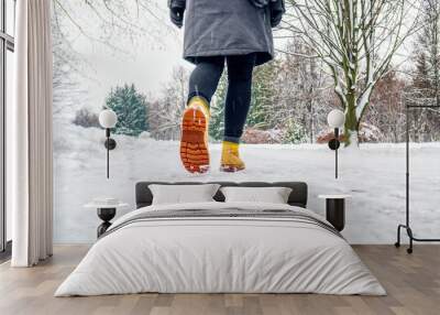 Winter Walk in Yellow Leather Boots. Back view on the feet of a women walking along the icy snowy pavement. Pair of shoe on icy road in winter. Abstract empty blank winter weather background Wall mural