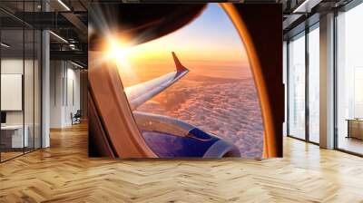 plane wing from airplane window seat in flight nature landscape against scenic sunset sky background. Aerial view from aircraft passenger cabin on beautiful red orange sunrise cloudscape and blue sky Wall mural