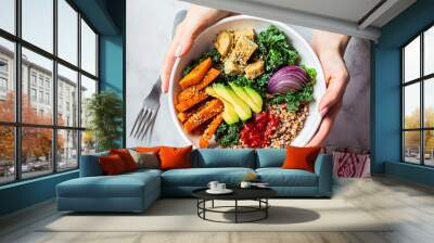 Woman hands eating vegan salad of baked vegetables, avocado, tofu and buckwheat buddha bowl, top view. Plant based food concept. Wall mural