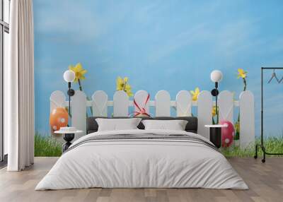 Spring grass and wooden fence with narcissus and easter decoration on cloudy sky Wall mural