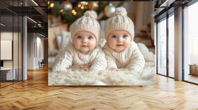 Two cute baby twins in white knitted hats on Christmas tree background Wall mural