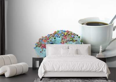 View of a sweet donut with blue icing and crushed candies. Donut on a white background with a cup of hot coffee. Sweet dish. Ready to eat. Sweet decorated donut filled with chocolate. Wall mural